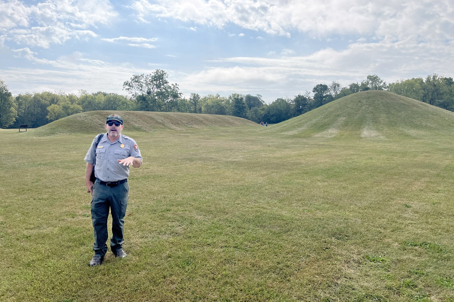 An NPS archaeologist speaks animatedly near a pronounced, almost conical mound. 